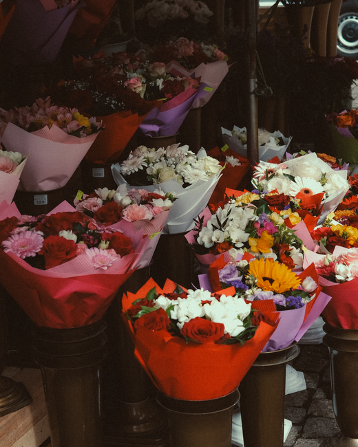 A display of multiple floral bouquets arranged in various wrapping papers, including pink, white, red, and purple, each featuring a diverse selection of fresh flowers such as roses, daisies, tulips, a