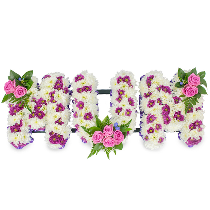 This intimate, mournful composition reads as a tactile message of love: the letters MUM, formed in three strong, three-dimensional capitals against a neutral white background. Each letter is composed of a densely packed bed of snowy white chrysanthemums, their small, rounded petals layered to create a velvety, cloud-like surface that catches soft studio light and emphasises texture. Dotted throughout the white are vibrant pockets of magenta and deep purple spray chrysanthemums, applied with restraint to create contrast without overwhelming the calming base. The bouquet architecture is carefully considered: bright pink spray roses punctuate the design in three deliberate clusters - a delicate grouping at the upper left of the first M, a larger, more central bouquet cradled inside the lower curve of the U, and a reflective cluster at the upper right of the final M. Sprays of verdant foliage and fern fronds fan out behind these rose clusters, offering cooler tones and a sense of shelter; here and there, very small blue accent blooms peek out, adding a soft, cool counterpoint to the warm pinks. A subtle dark horizontal bar links the letters and provides a discreet framework while a narrow purple ribbon follows parts of the letters' contours, lending a refined edge. In gentle light the chrysanthemums show their creamy warmth and the roses project a tender scent; the overall mood is one of respectful remembrance, a bespoke sympathy piece that balances classical white with thoughtful colour. Suitable for funerals, wakes or memorial displays, this tribute demonstrates the attentive craftsmanship and empathetic design families expect from a trusted local florist serving the Yiewsley community.