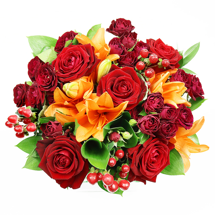 Captured directly from above on a crisp white background, this luxurious bouquet is a study in contrast and warmth, handcrafted in our Yiewsley studio at Flowers Yiewsley. A cluster of large, fully opened deep red roses anchors the design, their velvety petals unfolding in concentric layers that speak of classic romance and thoughtful intention. Interwoven through the arrangement are vivid orange Asiatic lilies - some wide open with stamens exposed and others in coy, unfolding stages - their trumpet forms creating dynamic focal points and a burst of warmth. Companioning these are abundant spray roses in a rich burgundy tone; their smaller, tightly packed heads add tactile depth and a jewel-like density that balances the larger roses. Glossy hypericum berries, the colour of ripe cranberries, dot the bouquet with cheerful pops and catch light to create tiny points of visual excitement. Surrounding and lifting the flowers, broad green foliage such as ruscus or salal provides a fresh, cooling contrast and frames the rounded silhouette, giving the bouquet volume and an organic rhythm. The soft, even lighting highlights the interplay of textures - velvet petals, satiny leaves, and glassy berries - and the imagined scent is layered: warm rose notes undercut by the lively, citrus-spicy lift of lilies. This arrangement reads as both festive and intimate, perfect for anniversaries, romantic gestures, or as a tasteful centrepiece for a home near Yiewsley Market or a sunny table at Colham Green, expressing warmth, celebration, and considered floral artistry.