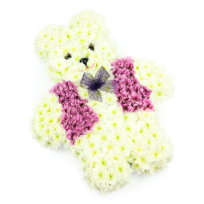 A sweet teddy bear formed entirely from fresh flowers is the focus of this serene funeral tribute, its body built from layers of soft white and pale ivory chrysanthemums that mimic the look of plush fur. The florist has sculpted the figure with remarkable precision: the head is rounded and slightly tilted, the ears stand forward in friendly curves, and the arms and legs are short and stout, giving the bear a reassuring, cuddly stance. In the centre of the face, two dark, bead-like eyes and a matching triangular nose create a simple, open expression, as if the bear is quietly keeping watch. A faint suggestion of a smile is created with a delicate line of lighter petals, adding warmth and innocence. Across the chest, a waistcoat effect is created using clusters of deep pink and magenta blossoms, arranged in clear, symmetrical panels that resemble little lapels. This darker, richer colour band contrasts beautifully with the surrounding creamy blooms, drawing the eye to the centre of the design. Nestled at the top of the vest sits a small bow made from fine violet netting, its soft folds and see-through texture lending a hint of playfulness and grace. The piece is photographed in bright, neutral light against a white background, highlighting every petal and curve without distraction. Crafted for families in Yiewsley and nearby Hayes or Harlington, this floral teddy bear feels especially meaningful as a tribute for a young life, a baby's memorial, or a gentle farewell that offers comfort and cherished memories through flowers.